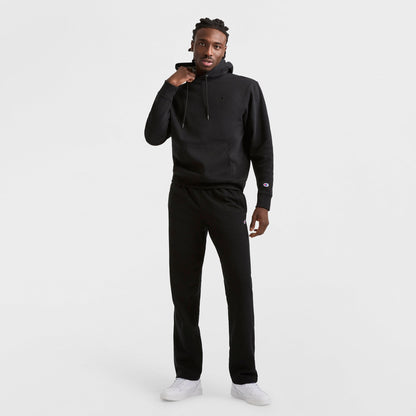Against a plain white background, a person wears Champion Powerblend Sweatpants, Open Hem, C Logo, paired with a black hoodie and white sneakers. They raise one hand to their chin and look at the camera.