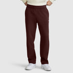 A person wearing maroon Champion Powerblend Sweatpants, Relaxed Bottom, C Logo, paired with a cream sweater and white sneakers, stands with hands in pockets against a plain light gray background.