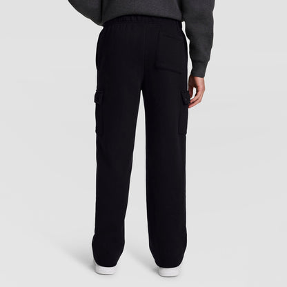 A person is seen from the back wearing Champion’s Fleece Cargo Pant, C Logo, styled with a dark sweatshirt. The black pants feature side and back pockets and are crafted from a comfortable cotton-polyester fleece fabric. The individual is standing on a plain light background.