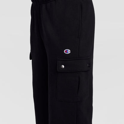 Close-up of the Champion Fleece Cargo Pant, C Logo in black streetwear style, featuring a cargo pocket with snap buttons. The signature Champion C logo patch is displayed above the pocket. The background is plain and light-colored.