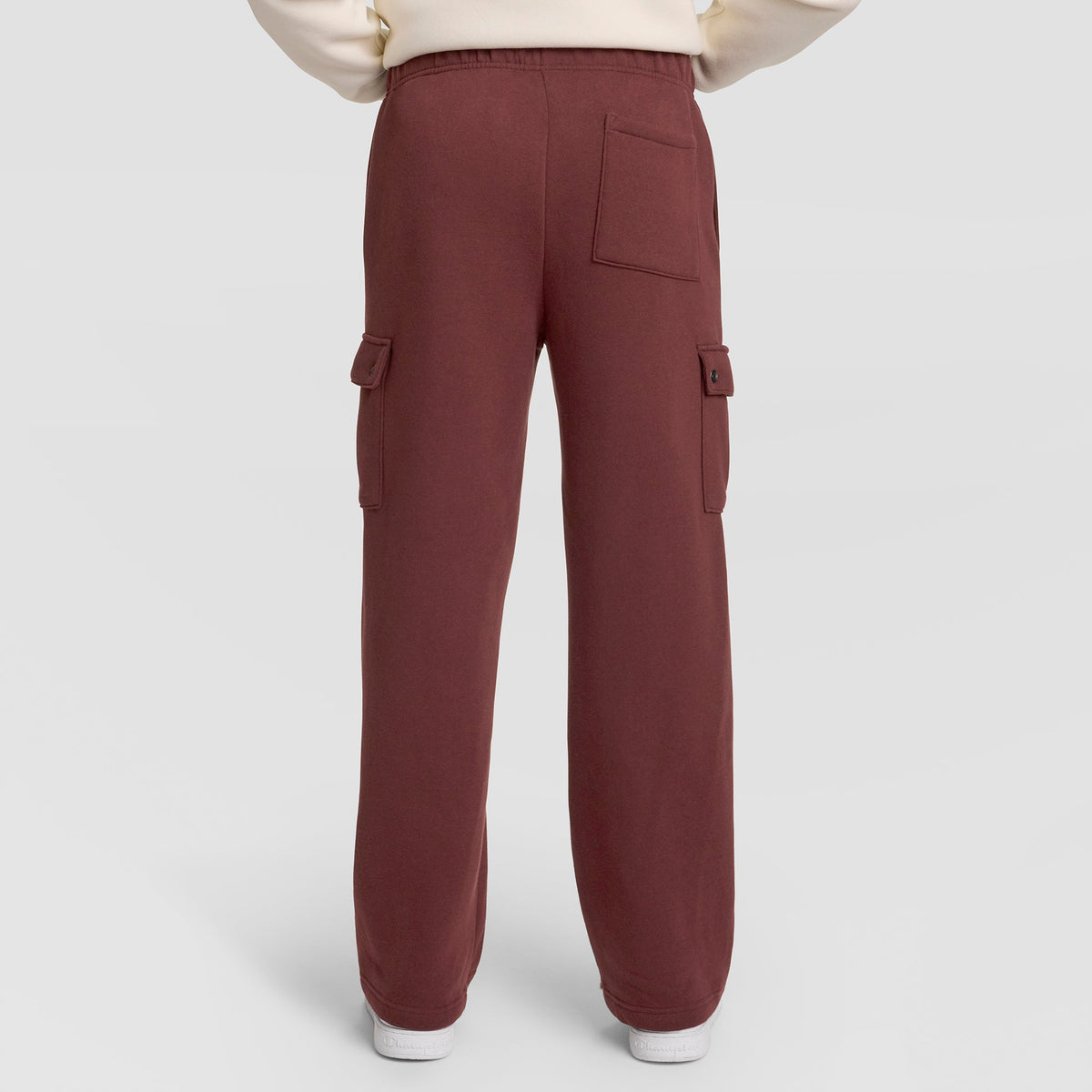 A person wearing Champion Fleece Cargo Pant, C Logo in maroon, styled as streetwear with side and back pockets, stands against a plain light background. Only the lower half of the body is visible.
