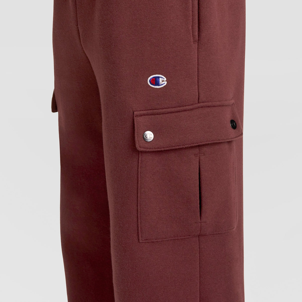 Side view of the Champion Fleece Cargo Pant, C Logo in maroon, featuring classic cargo pant styling with a buttoned flap pocket and a small C logo patch above the pocket—ideal for streetwear enthusiasts.
