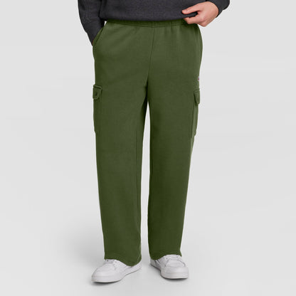 Dressed in Champion’s Fleece Cargo Pant, C Logo—a stylish olive green men’s cargo sweatpant inspired by streetwear—this individual pairs the look with a dark sweatshirt and white sneakers, standing with one hand in a pocket against a plain background.