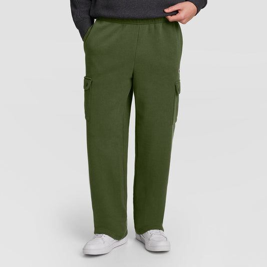 Dressed in Champion’s Fleece Cargo Pant, C Logo—a stylish olive green men’s cargo sweatpant inspired by streetwear—this individual pairs the look with a dark sweatshirt and white sneakers, standing with one hand in a pocket against a plain background.