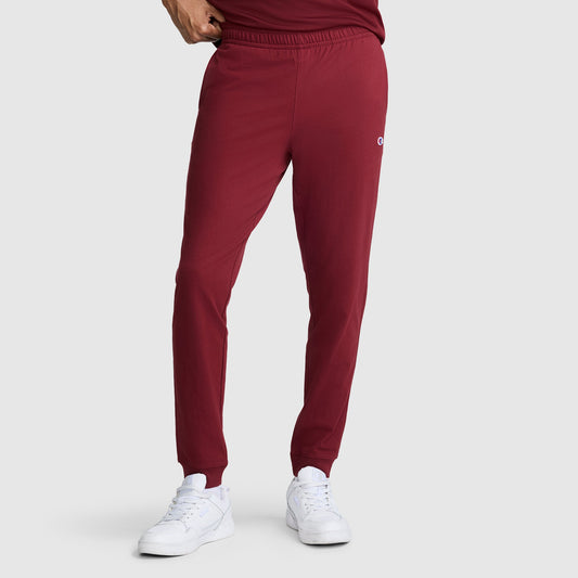 A person is shown from the waist down wearing Champion Lightweight Lounge Joggers, C Logo in maroon and white sneakers, standing against a plain light gray background.