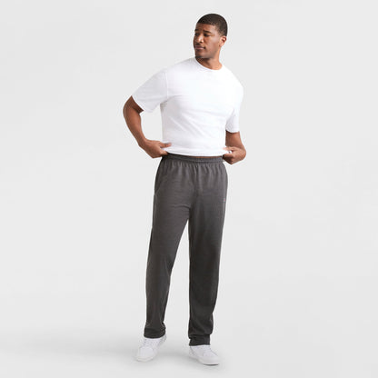 A man stands against a white background, wearing a white T-shirt, Champion Lightweight Lounge Pants with Open Hem and C Logo (Big & Tall) in dark gray, and white sneakers. He looks left, holding his shirt’s hem with both hands.