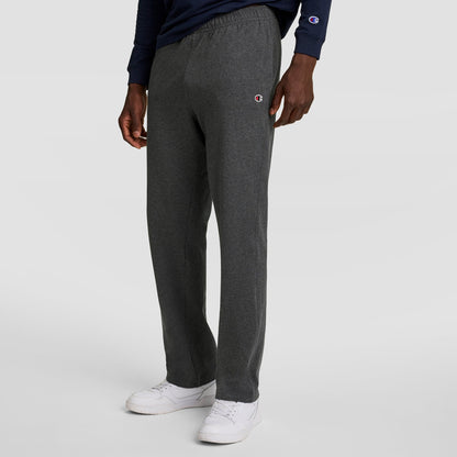 A person wearing dark gray Champion Lightweight Lounge Pants with an open hem and C logo, a navy long-sleeve shirt, and white sneakers stands against a plain light gray background.