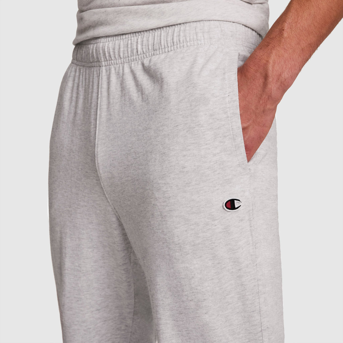 A person wears Champion Lightweight Lounge Pants with a cinched hem, their right hand in the pocket. These comfortable pants feature a stretch waistband and a visible C logo on the upper thigh.