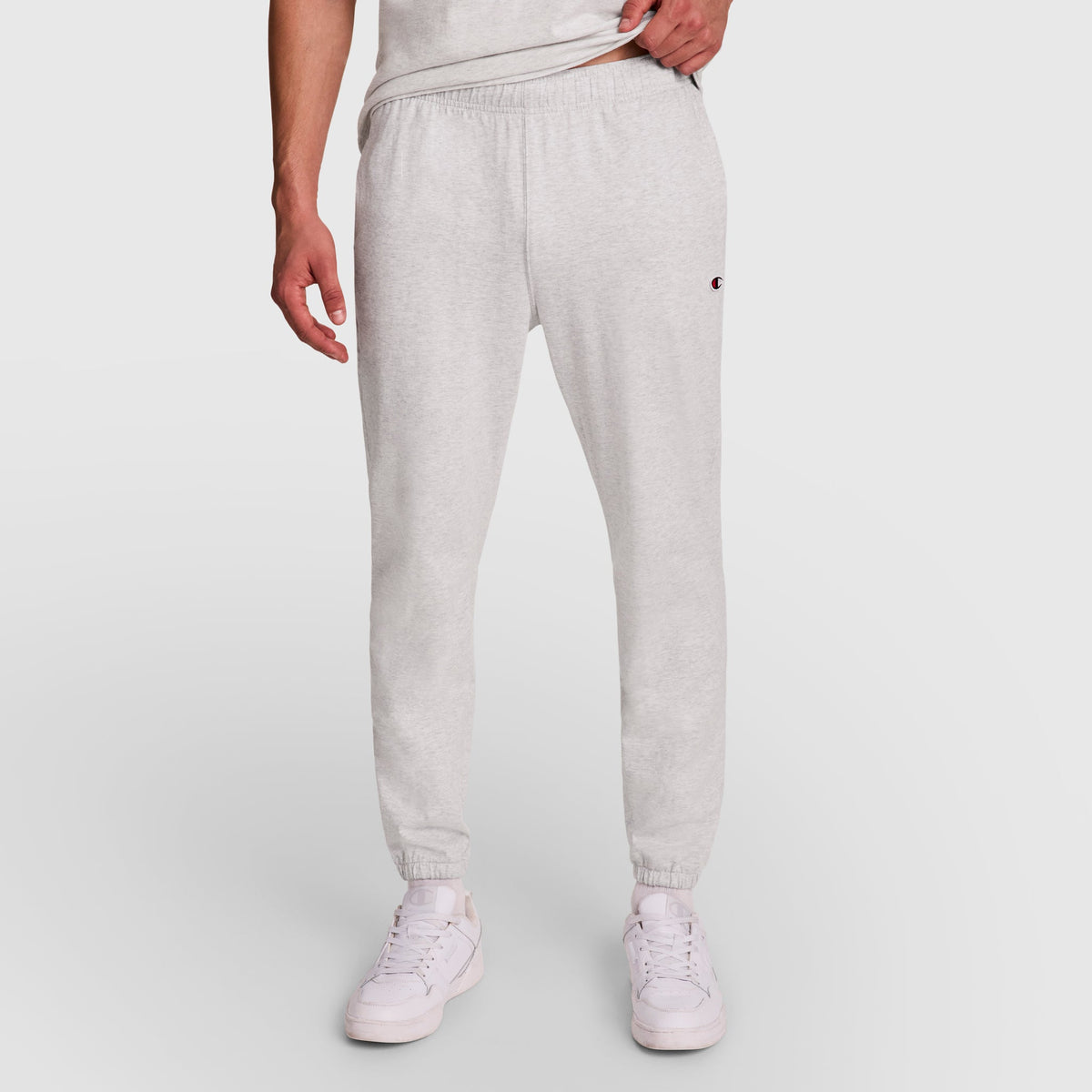 A person wears Champion Lightweight Lounge Pants with a stretch waistband, cinched hems, and a small C logo on the left thigh, paired with a matching tee and white sneakers against a plain white background.