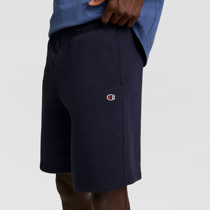 A person wearing navy blue Champion 10" Powerblend Fleece Shorts and a blue shirt, with only torso and legs visible against a plain background.