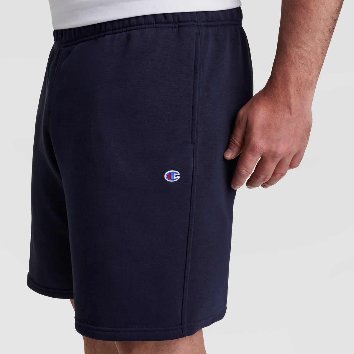 A person models the Champion 10" Powerblend Fleece Short - Big & Tall in navy blue with a small left leg logo, against a plain white background. Only their torso and upper legs are visible.
