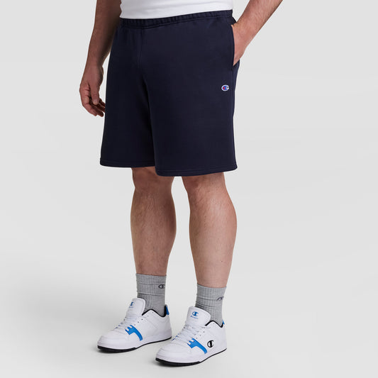 A person in navy Champion 10" Powerblend Fleece Short - Big & Tall, gray Champion socks, and white Champion sneakers with blue accents stands against a plain light background.