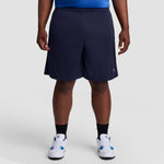 A person stands facing forward against a light gray background, showing only the lower half of their body. They are wearing Champion's 9" Classic Mesh Shorts, C Logo - Big & Tall, along with black socks and white sneakers.