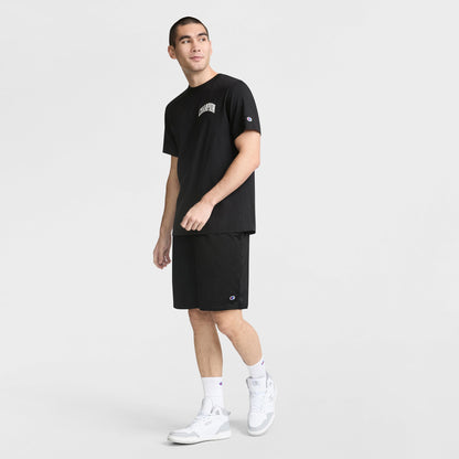 A person wearing a black Champion t-shirt, Champion 9" Classic Mesh Shorts with C Logo, white crew socks, and white sneakers stands against a plain white background looking to the side with one arm slightly raised.