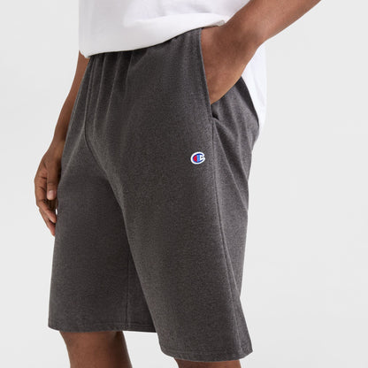 A person wearing a white shirt and Champion 9" Lightweight Lounge Shorts, C Patch Logo - Big & Tall in dark gray cotton jersey, with hands in pockets, shown from the waist down against a plain background.