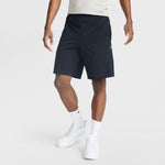 A person wearing a light gray t-shirt, Champion 9" Lightweight Lounge Shorts with the C Patch Logo in black cotton jersey, white socks, and white sneakers stands against a plain light background. Only the body from the shoulders down is visible.