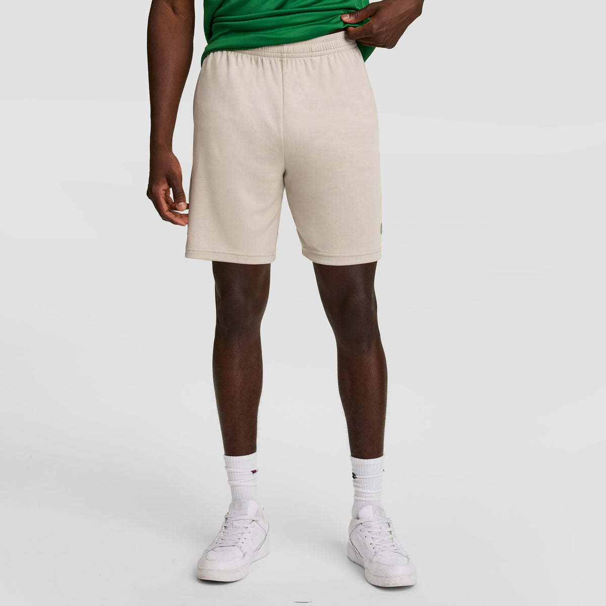 A person in a green shirt, Champion 7" Moisture Wicking Sport Shorts, white crew socks, and white sneakers stands against a plain light background. Their face is not visible.