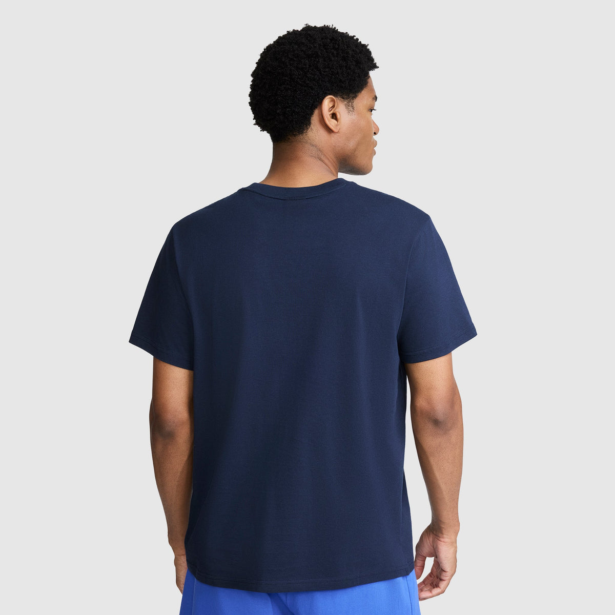 Back view of a person wearing a plain navy blue 100% cotton crew neck Classic Graphic T-Shirt, Tonal Script Logo by Champion.