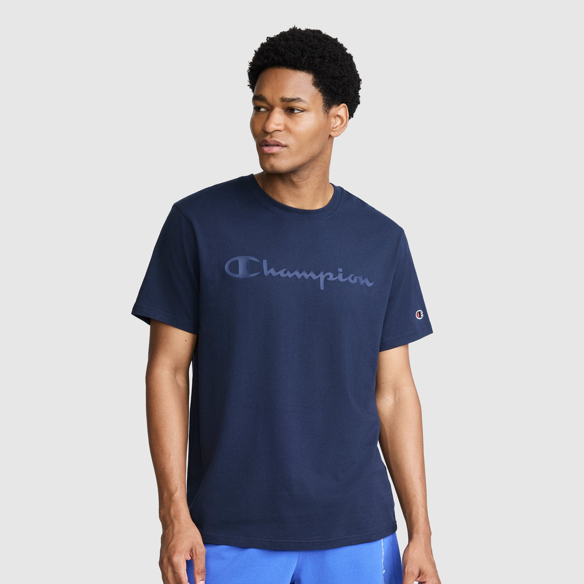 A man wearing a navy Classic Graphic T-Shirt, Tonal Script Logo with a tonal script logo across the chest.