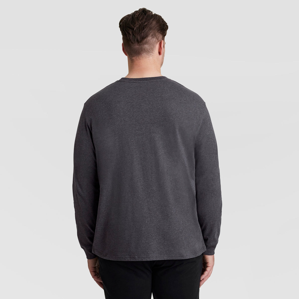 A man seen from behind wearing a charcoal gray Champion Classic Long Sleeve T-Shirt, Embroidered C Logo - Big & Tall and black pants.