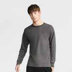 A young man with short brown hair wears a Champion Classic Long Sleeve T-Shirt with embroidered C logo in dark gray and black pants, standing against a light gray background.