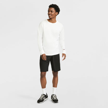 A man smiles, wearing a Champion Classic Long Sleeve T-Shirt with an embroidered C logo, black shorts, white socks, and black sneakers against a plain white background.