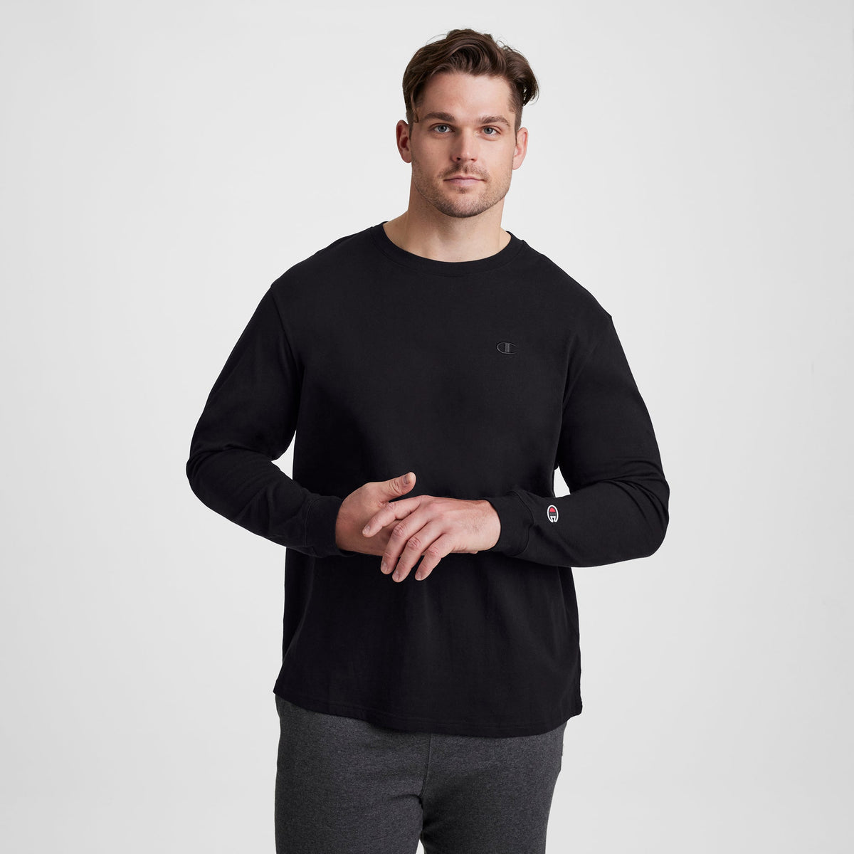 A man wearing a black Champion Classic Long Sleeve T-Shirt, Embroidered C Logo - Big & Tall, featuring a small embroidered logo on the chest and a patch on the sleeve.