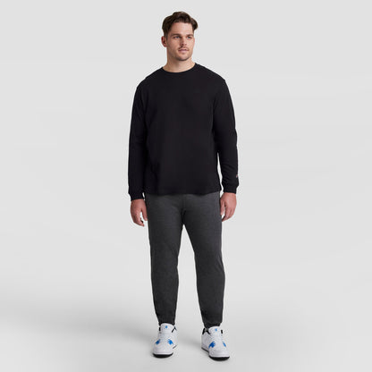 A man wears a Champion Classic Long Sleeve T-Shirt, Embroidered C Logo - Big & Tall, charcoal gray joggers, and white sneakers with blue accents.