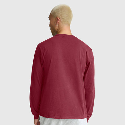 A person with short blond hair is shown from behind, wearing a Champion Classic Long Sleeve T-Shirt with an embroidered C logo in maroon and light gray pants against a plain light gray background.