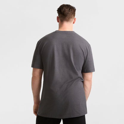 A man faces away from the camera, wearing a Champion Classic T-Shirt, C Logo - Big & Tall in dark gray with black pants, set against a plain white background.