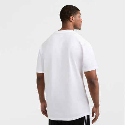 A man stands with his back to the camera, wearing a Champion Classic T-Shirt, C Logo - Big & Tall in white and black shorts with white stripes, set against a light gray background.