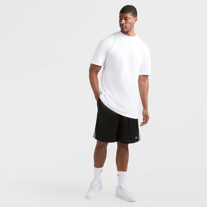A man stands against a white background wearing a Champion Classic T-Shirt, C Logo - Big & Tall, paired with black athletic shorts with white stripes, white crew socks, and sneakers. One hand is in his pocket as he looks to his left.