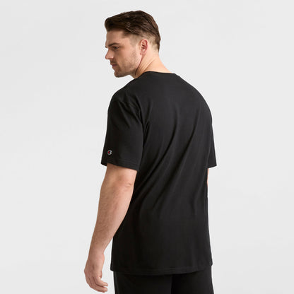 A man with short brown hair, a beard, and mustache stands slightly turned to the side, modeling the Champion Classic T-Shirt, C Logo - Big & Tall with black pants against a plain white background.