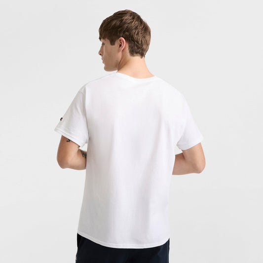 A young man with short brown hair stands with his back to the camera, wearing a Champion Classic T-Shirt, C Logo, and dark pants against a plain white background.