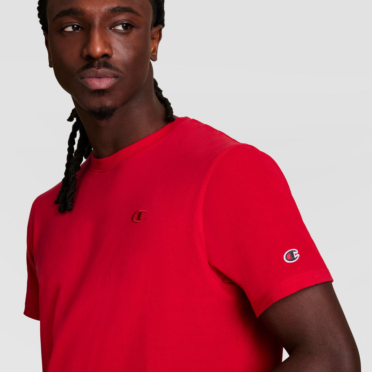 A man wearing a red Champion Classic T-Shirt, C Logo, featuring a small embroidered logo on the chest and a logo patch on the sleeve.