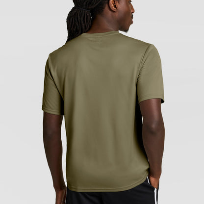 A man with long braided hair, seen from behind, wears a Champion Sport T-Shirt with Double Dry technology and a reflective C logo in olive green, paired with black shorts, standing against a plain light gray background.
