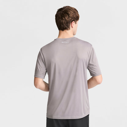 A person with short brown hair faces away, wearing a Champion Sport T-Shirt with a reflective C logo and Double Dry technology in light gray, paired with black pants against a plain white background.