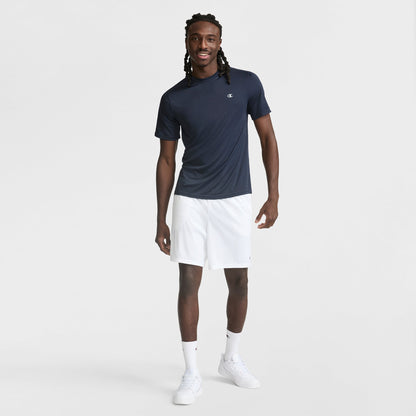A man with long twisted hair smiles against a plain white background, wearing a Champion Sport T-Shirt with Reflective C Logo featuring Double Dry technology, paired with white shorts, crew socks, and sneakers.