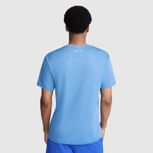 A person stands facing away, wearing a light blue Champion Sport T-Shirt with Reflective C Logo and matching blue shorts. The background is plain light gray.