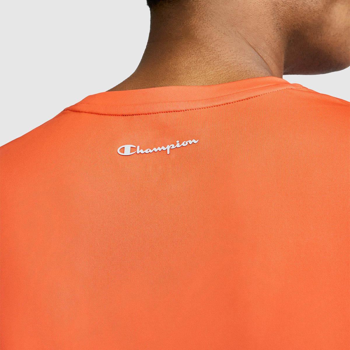 Close-up of a person wearing the orange Champion Sport T-Shirt with Reflective C Logo, showing only the back and part of their neck. The brand name “Champion” is printed in white near the collar.