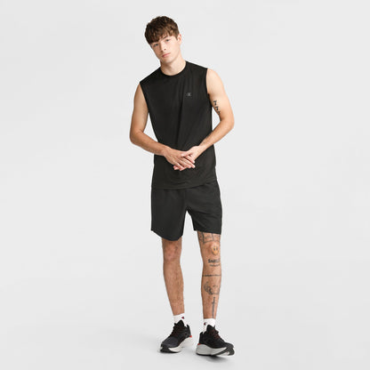 A young man wears the Champion Sport Muscle Tank with Reflective C Logo, paired with black shorts and sneakers. Standing against a white background, he shows off leg tattoos and short hair—an ideal workout shirt for comfort and style.