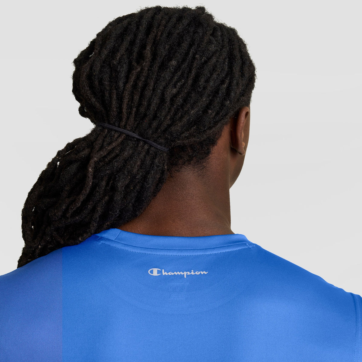 A person with long, dark dreadlocks tied back is seen from behind wearing the Champion Sport Muscle Tank with a Reflective C Logo against a plain, light background.
