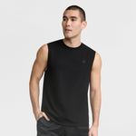A man with short dark hair wears a black Champion Muscle Tank (C Logo) and black shorts, standing with one hand in his pocket against a plain white background.