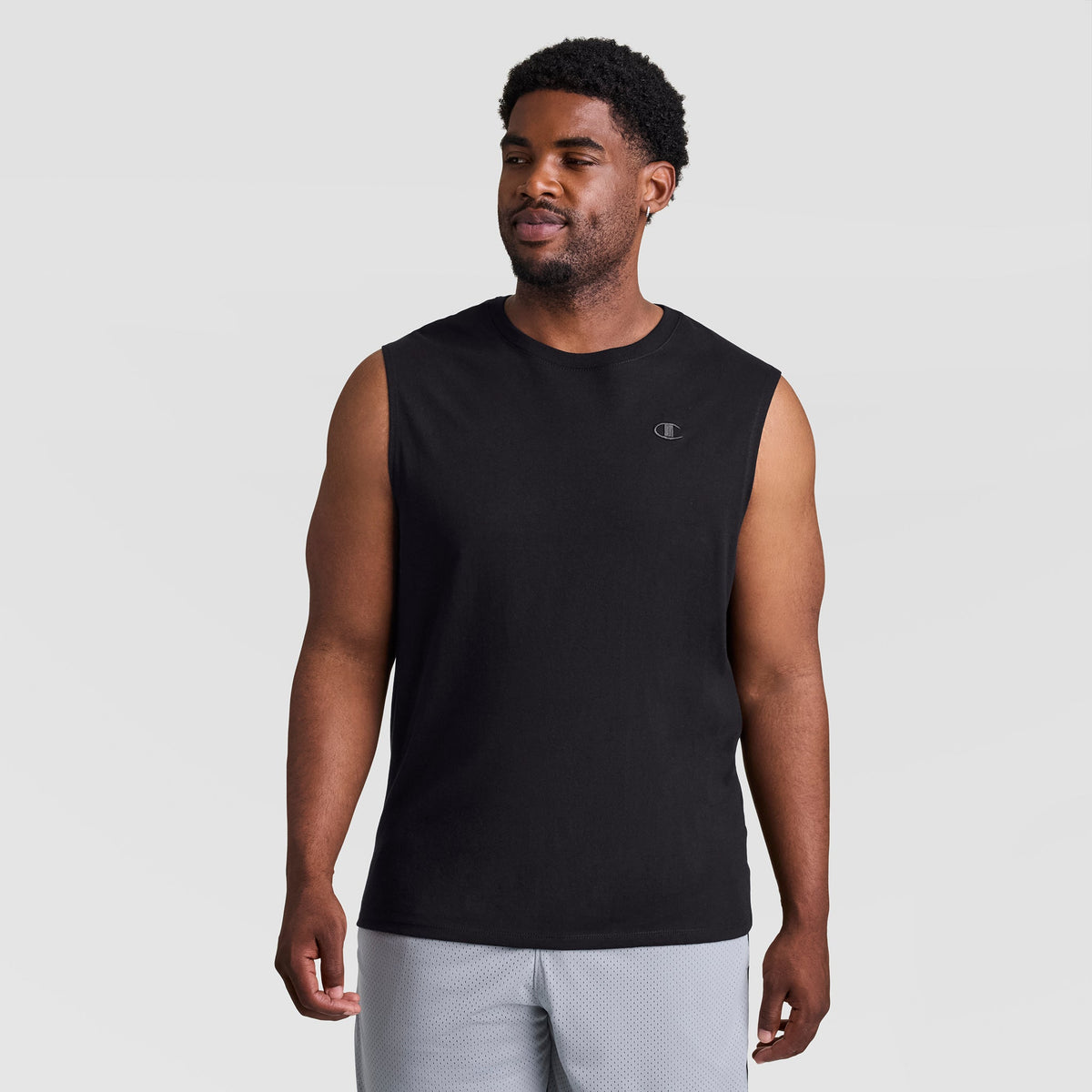 A man wearing a black Muscle Tank, C Logo - Big & Tall with a small logo on the chest and light gray shorts.