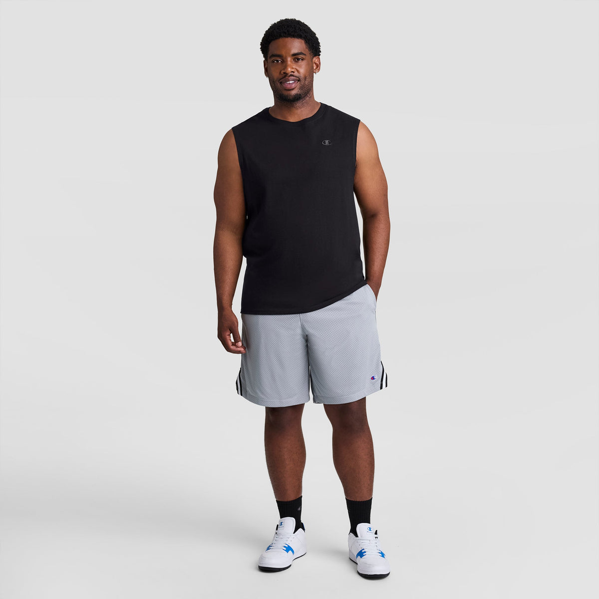 A man wearing a black Muscle Tank, C Logo - Big & Tall, grey athletic shorts, black socks, and white sneakers.