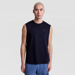 A person with short, light blond hair models the Champion Muscle Tank, C Logo—a sleeveless black top—paired with blue shorts against a plain light gray background, looking straight at the camera with a neutral expression.