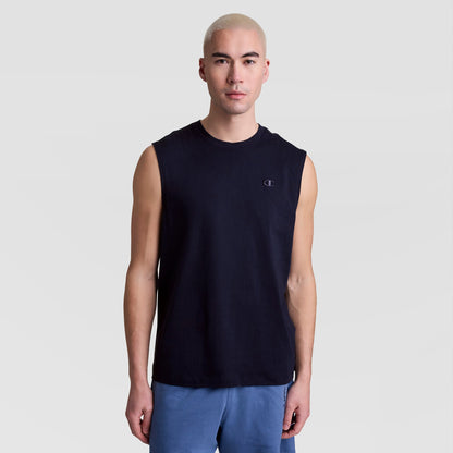 A person with short, light blond hair models the Champion Muscle Tank, C Logo—a sleeveless black top—paired with blue shorts against a plain light gray background, looking straight at the camera with a neutral expression.