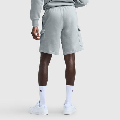 A person stands facing away, wearing Champion 8" Fleece Cargo Shorts with C Logo in light gray and a matching sweatshirt, plus white logo socks and white sneakers, against a plain background.