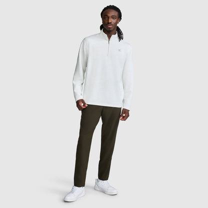 A man stands against a plain background wearing a light gray Champion Sport Long Sleeve 1/4 Zip Mockneck with the C Logo, paired with dark pants and white sneakers. His long hair is styled in twists, and he looks at the camera with a neutral expression.