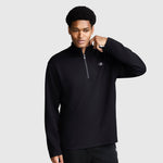 A man wears the Champion Sport Long Sleeve 1/4 Zip Mockneck featuring the signature C Logo in black, standing against a plain light gray background while holding the collar with one hand and gazing slightly to the side.